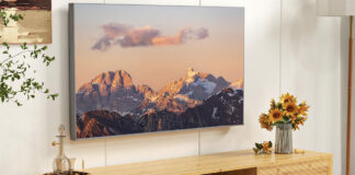 A TV mounted on the wall under a Costeay bamboo TV stand.