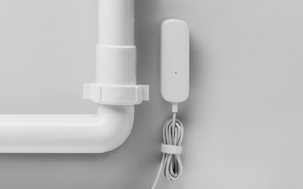 An Ooma water leak sensor mounted beside a pipe on a wall.